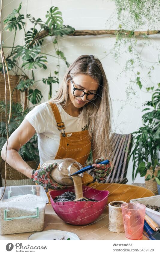 Junge Frau, die am Tisch in einem kleinen Gartenbaubetrieb arbeitet Job Berufe Berufstätigkeit Beschäftigung Jobs Blumentoepfe Blumentöpfe Tische Brillen Arbeit
