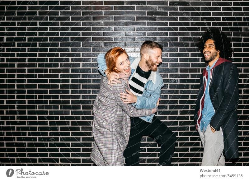 Drei glückliche verspielte Freunde an einer schwarzen Wand Glück glücklich sein glücklichsein Wände Waende stehen stehend steht schwarzer schwarzes spielerisch