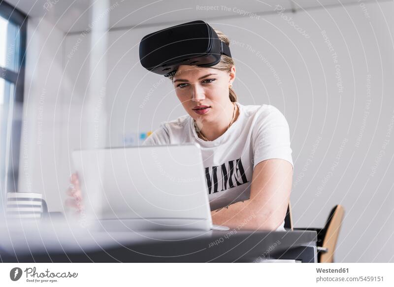 Junge Frau mit Laptop und VR-Brille bei der Arbeit am Schreibtisch im Büro Brillen weiblich Frauen arbeiten virtuell Virtualität Office Büros Notebook Laptops