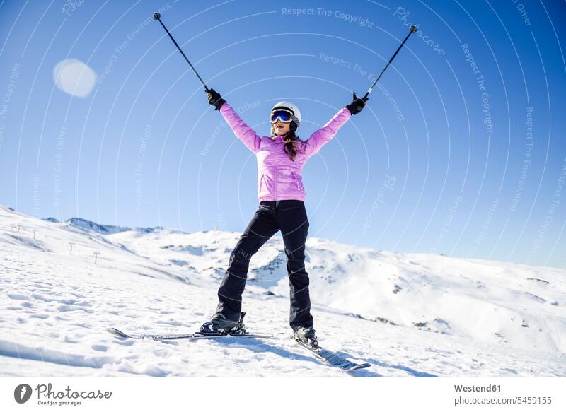 Glückliche Frau hebt ihre Skistöcke in verschneiter Landschaft in Sierra Nevada, Andalusien, Spanien Provinz Granada Skigebiet Skigebiete wolkenlos ohne Wolken