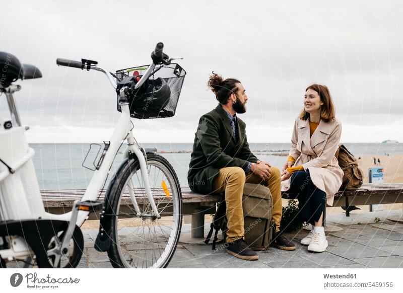 Paar sitzt auf einer Bank an der Strandpromenade neben dem E-Bike im Gespräch Strandpromenaden Stadt staedtisch städtisch eBikes E-Bikes Elektrofahrrad