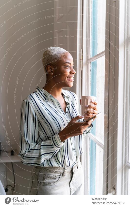 Glückliche Frau mit Handy und Kaffeetasse, die aus dem Fenster schaut geschäftlich Geschäftsleben Geschäftswelt Geschäftsperson Geschäftspersonen Businessfrau