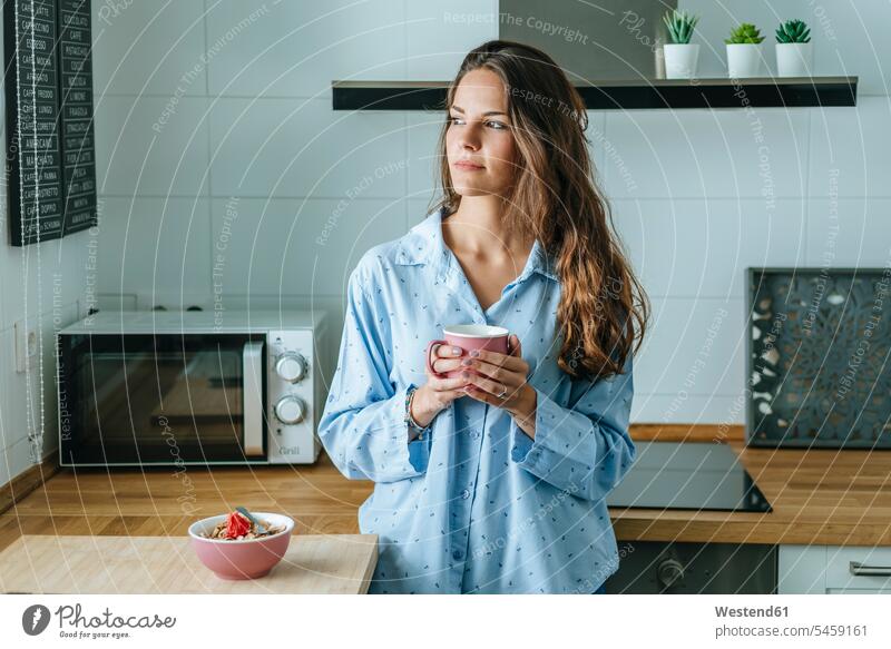 Porträt einer jungen Frau im Pyjama in der Küche zu Hause, die eine Tasse Kaffee hält Leute Menschen People Person Personen Europäisch Kaukasier kaukasisch 1