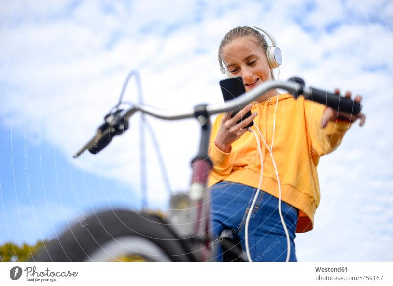 Lächelndes Mädchen mit Kopfhörer und Fahrrad schaut auf Smartphone Bikes Fahrräder Räder Rad weiblich iPhone Smartphones schauen sehend lächeln Kopfhoerer