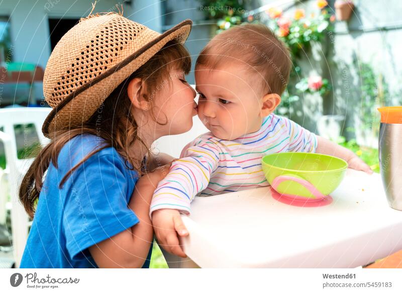 Kleines Mädchen küsst im Frühling ihre jüngere Schwester im Hinterhof Jahreszeiten Frühjahr Lenz sommerlich Sommerzeit gefühlvoll Emotionen Empfindung