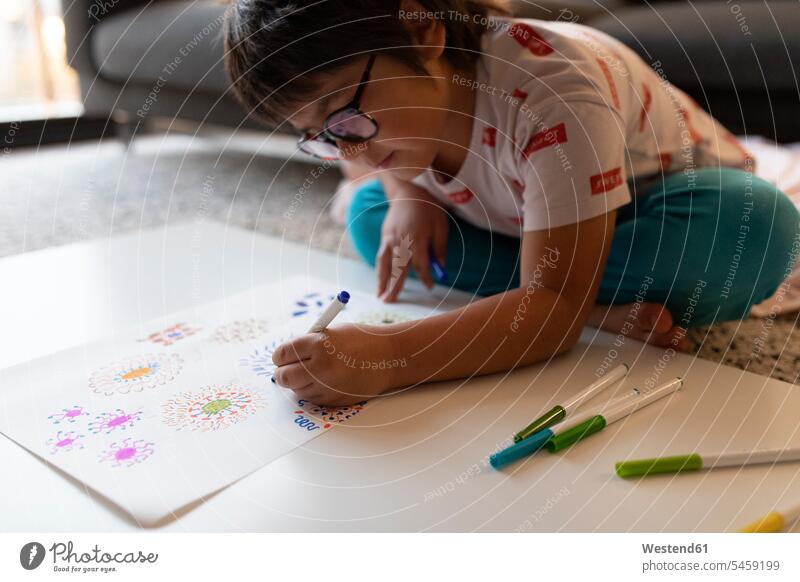 Junge sitzt zu Hause auf dem Boden und zeichnet Blumen Bilder Bildnis Zeichnungen Kinderzeichnungen Brillen sitzend daheim Muße konzentrieren konzentriert