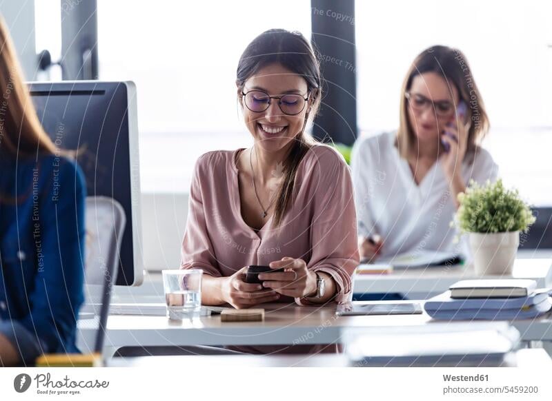 Lächelnde Geschäftsfrau kontrolliert Smartphone im Büro Job Berufe Berufstätigkeit Beschäftigung Jobs geschäftlich Geschäftsleben Geschäftswelt Geschäftsperson
