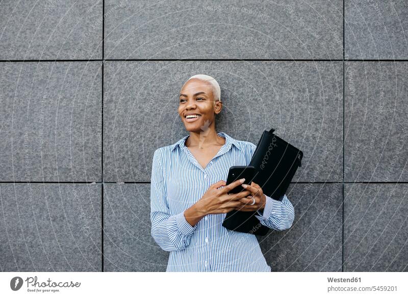 Lächelnde Geschäftsfrau mit Ordner und Telefon gegen Gebäude in der Stadt Farbaufnahme Farbe Farbfoto Farbphoto Außenaufnahme außen draußen im Freien Tag