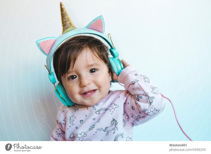 Porträt eines lächelnden Mädchens mit Einhornkopfhörern beim Musikhören Kopfhörer Kopfhoerer Baby Babies Babys Säuglinge Kind Kinder hoeren weibliche Babys