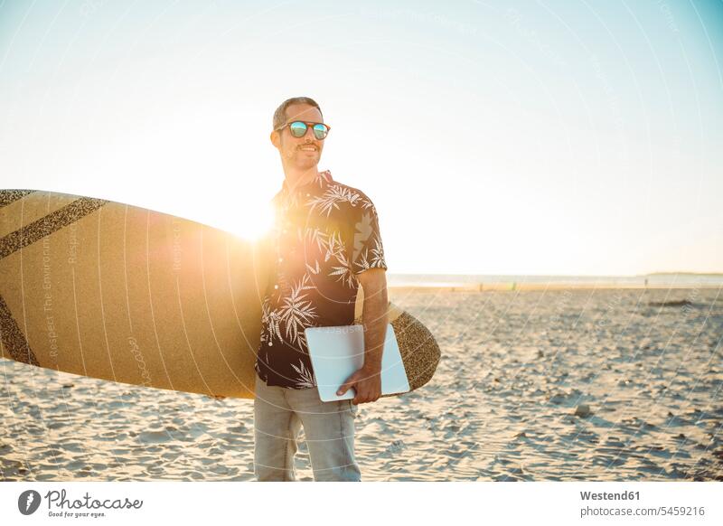 Mann am Strand trägt Surfbrett und Laptop Surfbretter surfboard surfboards Notebook Laptops Notebooks Beach Straende Strände Beaches tragen transportieren