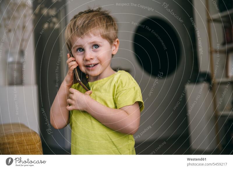 Porträt eines lächelnden kleinen Jungen am Telefon zu Hause T-Shirts Telekommunikation telefonieren Handies Handys Mobiltelefon Mobiltelefone hoeren Anruf