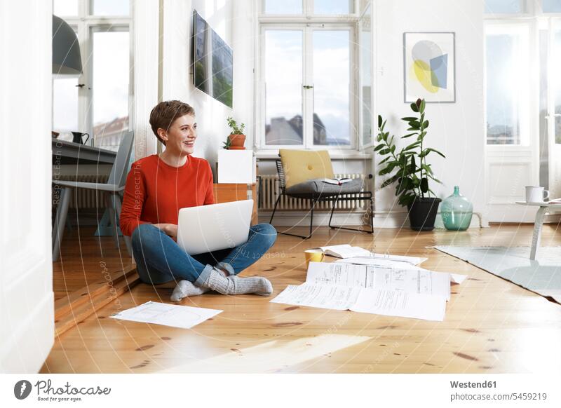 Frau sitzt im Schneidersitz auf dem Boden ihres Hauses und benutzt einen Laptop Laptop benutzen Laptop benützen arbeiten Arbeit sitzen sitzend Dokument