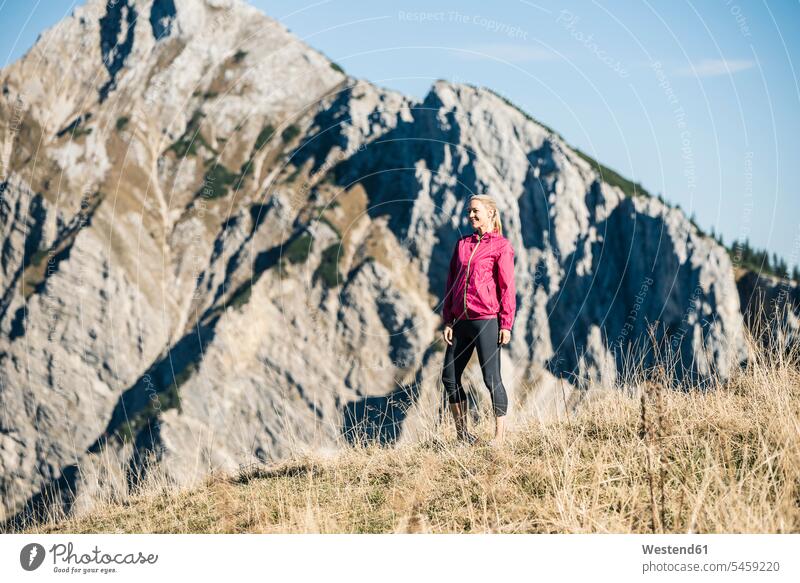 Österreich, Tirol, lächelnde Sportlerin auf Almwiese stehend Gebirge Berglandschaft Gebirgslandschaft Gebirgskette Gebirgszug Berge Sportlerinnen Frau weiblich