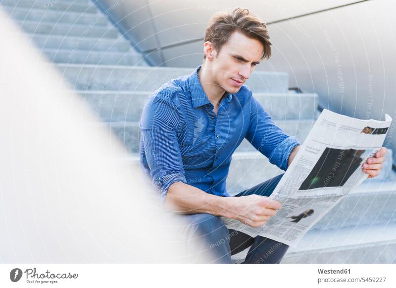 Selbstbewusster gutaussehender Geschäftsmann liest Zeitung, während er auf Stufen sitzt Farbaufnahme Farbe Farbfoto Farbphoto Deutschland Außenaufnahme außen