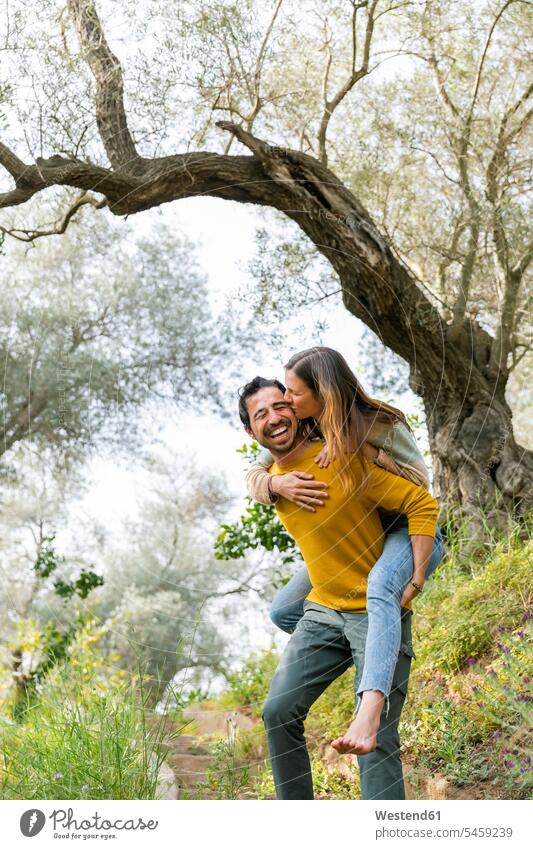 Fröhlicher Mann nimmt romantische Freundin huckepack, während er auf dem Land an Bäumen steht Farbaufnahme Farbe Farbfoto Farbphoto Spanien