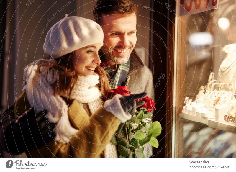 Lächelndes Paar, das in das Schaufenster eines Schmuckgeschäfts zur Weihnachtszeit schaut Pärchen Paare Partnerschaft Auslage Schmuckladen Juweliergeschaeft