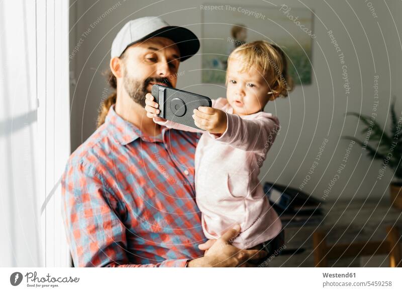 Vater hält seine kleine Tochter auf dem Arm und spielt mit seinem Smartphone iPhone Smartphones spielen Töchter Papas Väter Vati Vatis Papis tragen