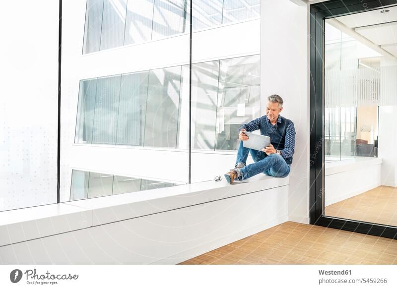 Gelegenheits-Geschäftsmann sitzt auf der Fensterbank eines Bürogebäudes und benutzt Laptp Leute Menschen People Person Personen Europäisch Kaukasier kaukasisch