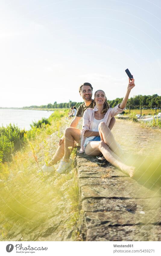 Glückliches Paar am Flussufer im Sommer, das ein Selfie macht glücklich glücklich sein glücklichsein Selfies Sommerzeit sommerlich Fluesse Fluß Flüsse Pärchen