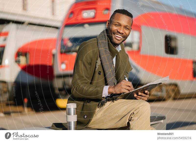 Porträt eines glücklichen Geschäftsmannes mit wiederverwendbarem Becher und Dokumenten, der auf den Zug wartet Job Berufe Berufstätigkeit Beschäftigung Jobs