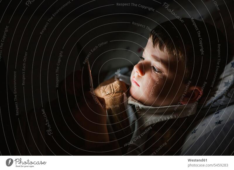 Porträt eines kleinen Jungen, der nachts mit seinem Smartphone im Bett liegt Leute Menschen People Person Personen Europäisch Kaukasier kaukasisch 1 Ein