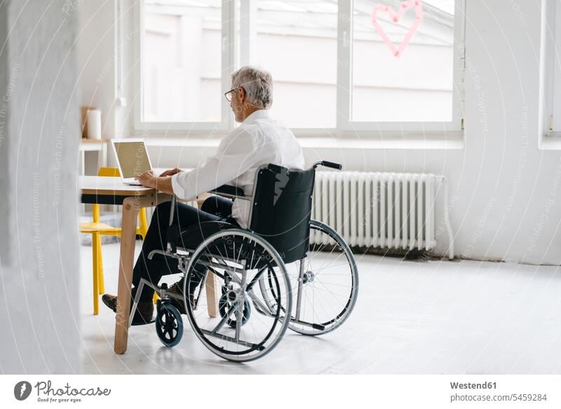 Behinderter Manager im Rollstuhl, arbeitet im Büro Laptop benutzen Laptop benützen Erfolg Erfolge erfolgreich Office Büros sitzen sitzend sitzt arbeiten Arbeit