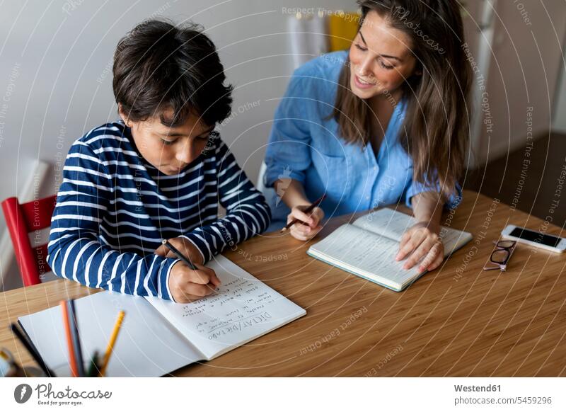 Junge Frau hilft dem Jungen zu Hause beim Schreiben von Hausaufgaben auf dem Tisch Farbaufnahme Farbe Farbfoto Farbphoto Spanien Freizeitkleidung