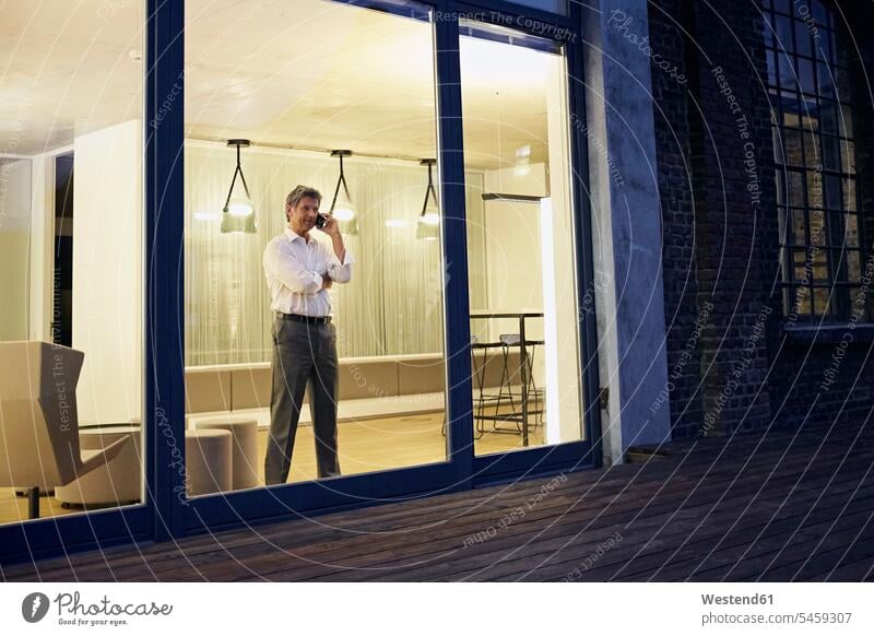 Außenansicht eines Mannes, der nachts ein Smartphone in einem modernen Gebäude benutzt iPhone Smartphones Geschäftsmann Businessmann Businessmänner