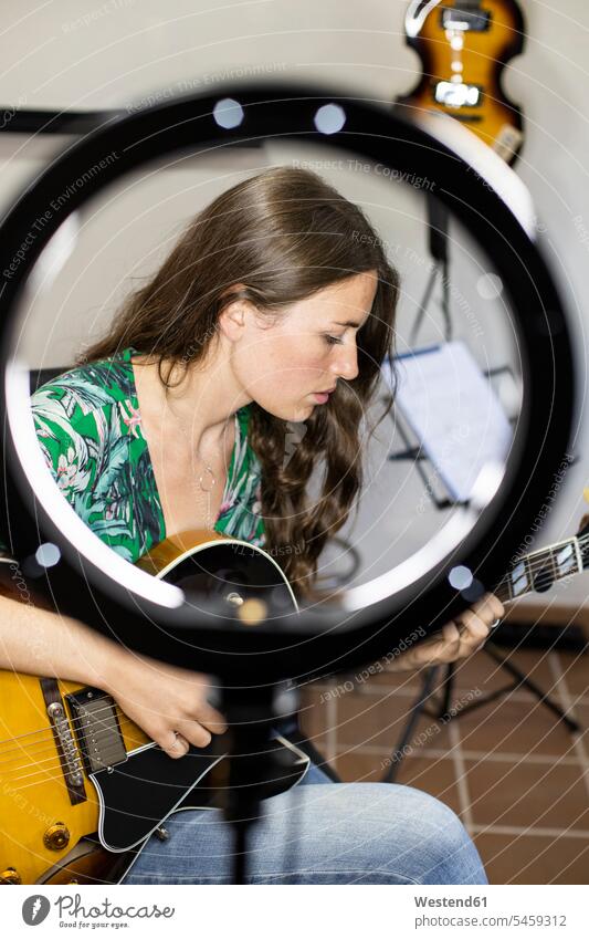 Junge Frau mit Webcam Licht Gitarre spielen, während zu Hause sitzen Farbaufnahme Farbe Farbfoto Farbphoto Innenaufnahme Innenaufnahmen innen drinnen