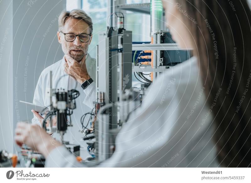 Nachdenklicher männlicher Wissenschaftler betrachtet Maschinen, während er mit einer Kollegin im Labor arbeitet Farbaufnahme Farbe Farbfoto Farbphoto