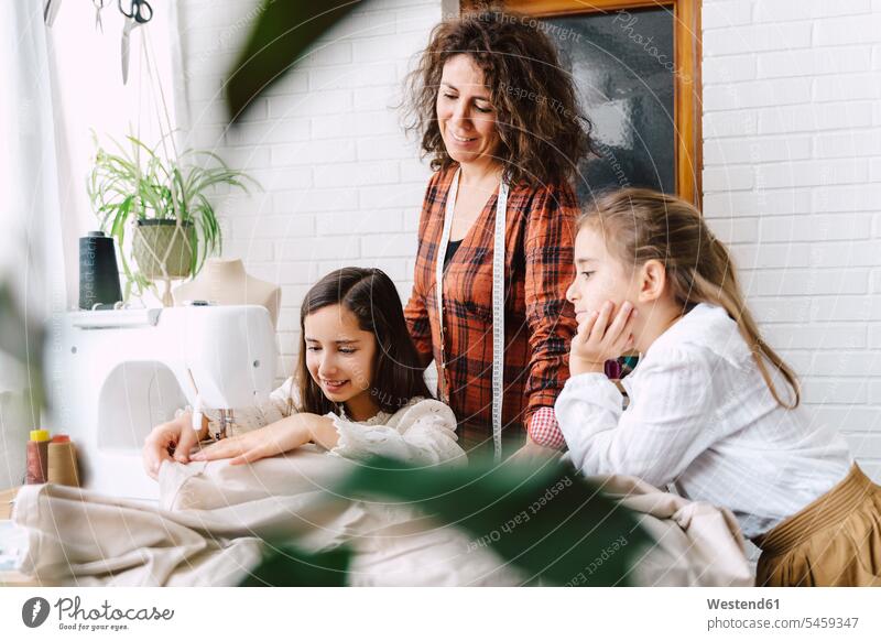 Mutter und zwei Töchter nähen zu Hause Massband Messband Metermaß Tische Textilien Gewebe Stoffe Textilfasern naehen freuen daheim Miteinander Zusammen Kreativ