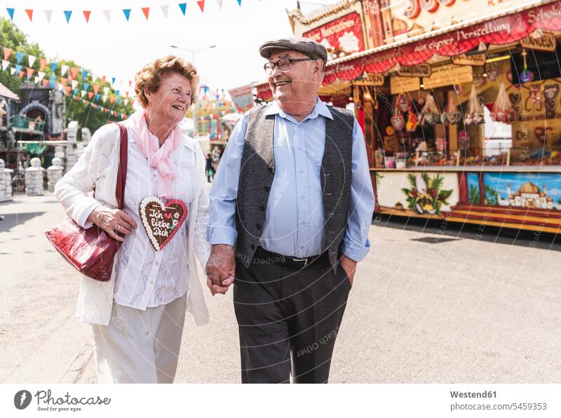 Glückliches älteres Ehepaar geht Hand in Hand auf dem Jahrmarkt Seniorenpaar älteres Paar Seniorenpaare ältere Paare Seniorenpärchen Volksfest gehen gehend