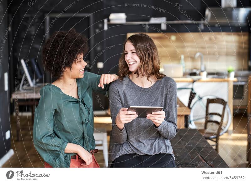 Zwei lachende junge Frauen mit Tablette im Büro Office Büros Tablet Computer Tablet-PC Tablet PC iPad Tablet-Computer weiblich Arbeitsplatz Arbeitsstätte