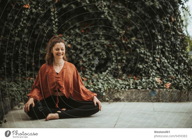 Frau praktiziert Yoga vor einer Wand mit Efeu sitzend sitzt entspannen relaxen entspanntheit relaxt freuen Glück glücklich sein glücklichsein zufrieden Muße
