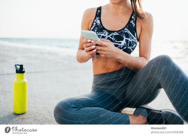 Niedriger Anteil einer jungen Frau, die nach dem Sport auf der Promenade ein Mobiltelefon benutzt Außenaufnahme außen draußen im Freien Tag Tageslichtaufnahme
