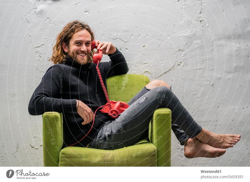 Lächelnder Mann spricht am Telefon, während er sich auf einem Sessel an der Wand entspannt Farbaufnahme Farbe Farbfoto Farbphoto Spanien Freizeitbeschäftigung