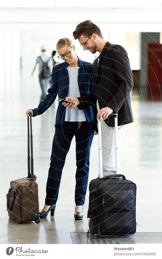 Zwei lächelnde junge Geschäftspartner mit einem Smartphone am Flughafen geschäftlich Geschäftsleben Geschäftswelt Geschäftsperson Geschäftspersonen