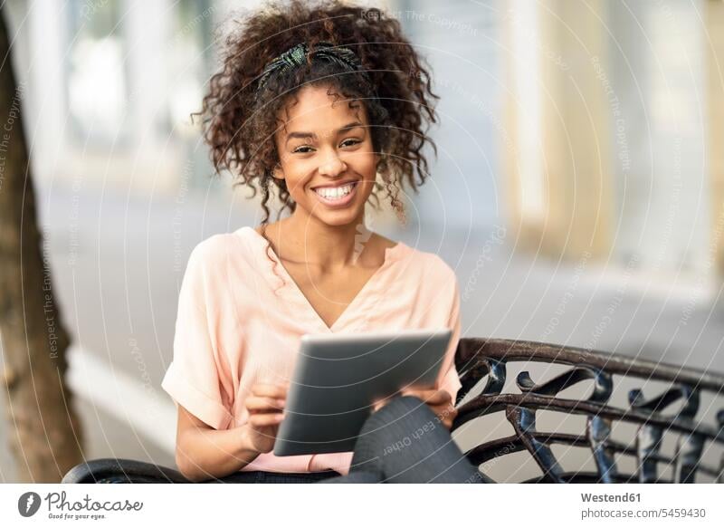 Porträt der glücklichen jungen Frau sitzt auf einer Bank mit Tablette Glück glücklich sein glücklichsein weiblich Frauen Portrait Porträts Portraits