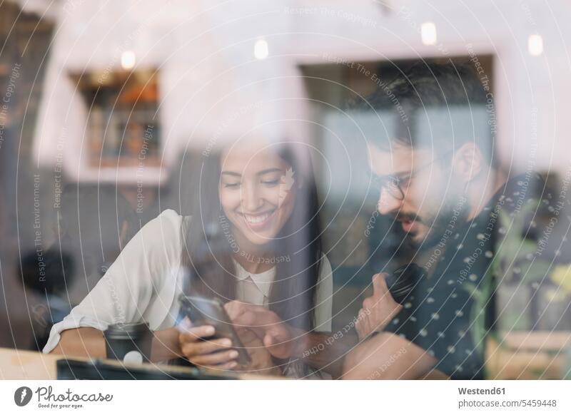 Junges Paar mit Smartphone hinter Fensterscheibe in einem Cafe Leute Menschen People Person Personen Europäisch Kaukasier kaukasisch 2 2 Menschen 2 Personen