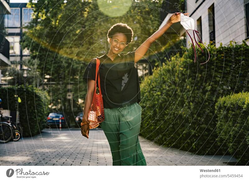 Porträt einer lächelnden jungen Frau mit Textilschutzmaske Taschen Einkaufstaschen Brillen Textilien Gewebe Stoffe Textilfasern freuen Glück glücklich sein