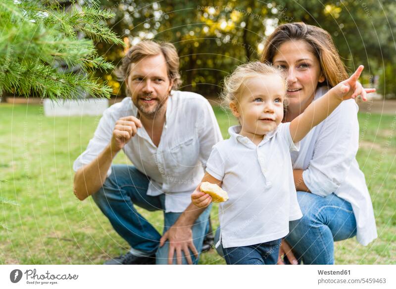 Eltern mit einer kleinen Tochter, die mit dem Finger auf eine Wiese zeigt Leute Menschen People Person Personen Europäisch Kaukasier kaukasisch