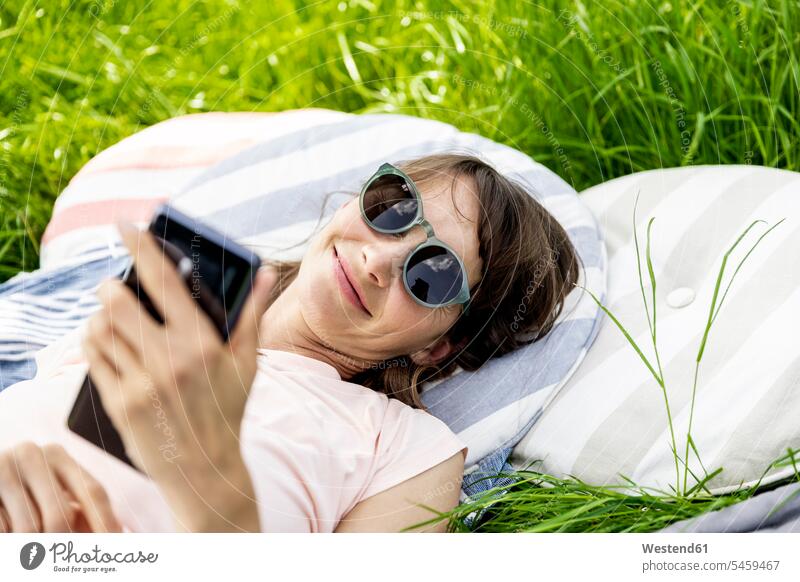 Entspannte Frau, die auf einer Wiese liegt und ein Mobiltelefon benutzt Leute Menschen People Person Personen Europäisch Kaukasier kaukasisch 1 Ein ein Mensch