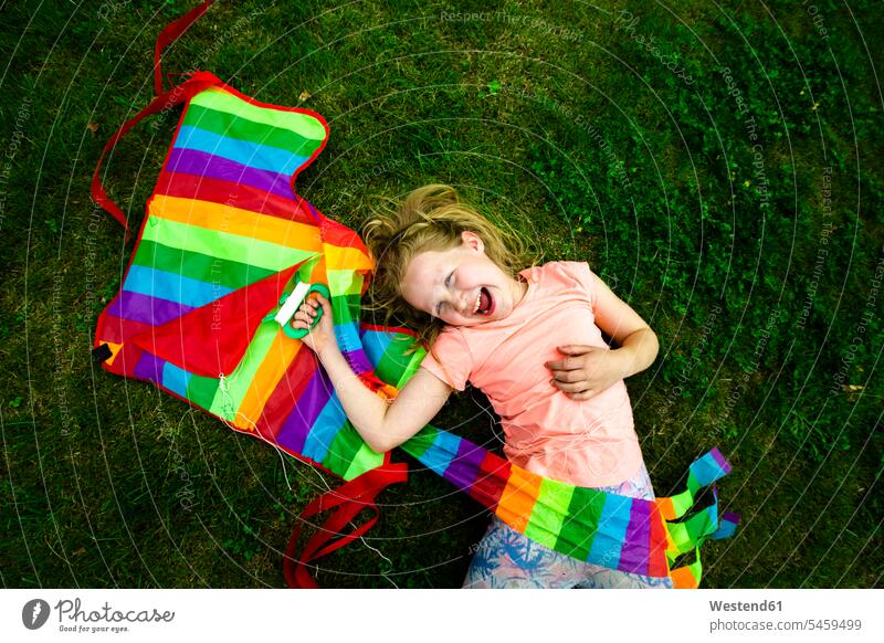 Glückliches Mädchen hält bunten Drachen, während sie im Park liegt Farbaufnahme Farbe Farbfoto Farbphoto Außenaufnahme außen draußen im Freien Tag