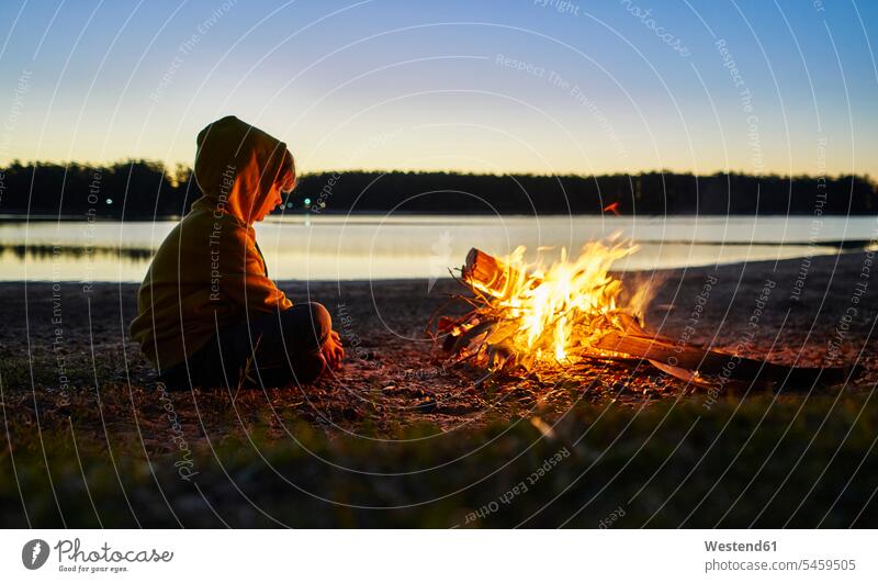 Argentinien, Patagonien, Concordia, Junge sitzt am Lagerfeuer an einem See Seen Buben Knabe Jungen Knaben männlich sitzen sitzend Gewässer Wasser Kind Kinder