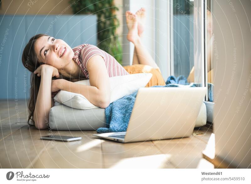 Entspannte junge Frau liegt am Fenster zu Hause mit Laptop liegen liegend Zuhause daheim weiblich Frauen entspannt entspanntheit relaxt lächeln Erwachsener