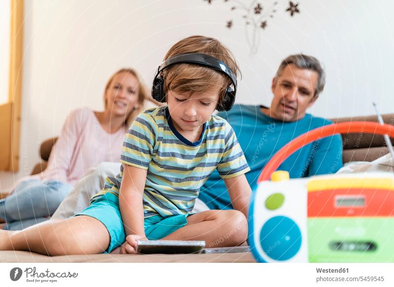 Familie zu Hause auf der Couch mit einem Jungen, der mit Kopfhörern Musik hört Couches Liege Sofas Kopfhoerer Radiogeraet Radiogerät Radios Medium CD ROM