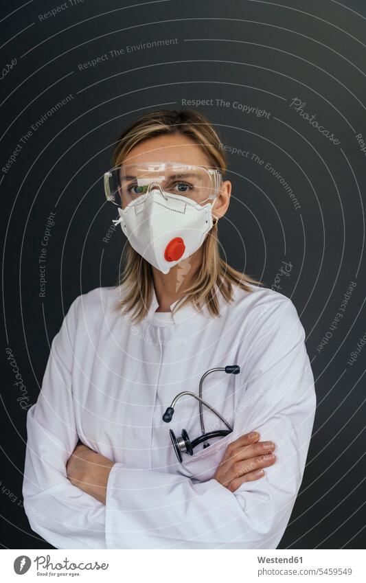 Porträt eines Arztes mit FFP3-Maske und Schutzbrille vor grauem Hintergrund Job Berufe Berufstätigkeit Beschäftigung Jobs Berufsbekleidung Gesundheit
