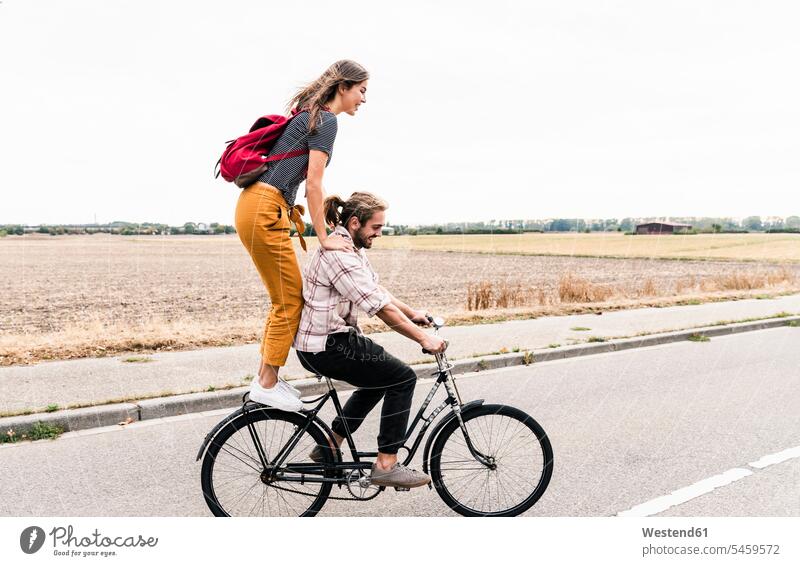 Glückliches junges Paar fährt gemeinsam auf einem Fahrrad auf der Landstraße Bikes Fahrräder Räder Rad fahren Gemeinsam Zusammen Miteinander glücklich