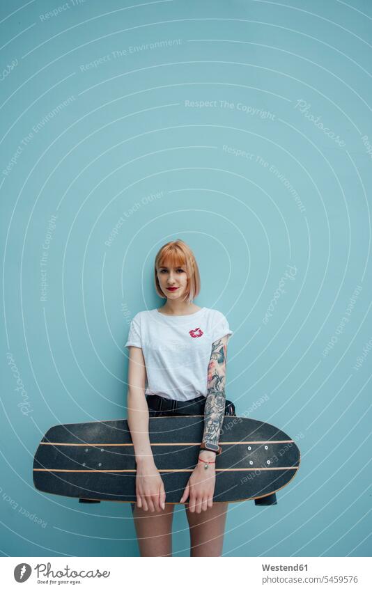 Porträt einer coolen jungen Frau, die ein Carver-Skateboard hält und an einer türkisfarbenen Wand steht stehen stehend Portrait Porträts Portraits Coolness