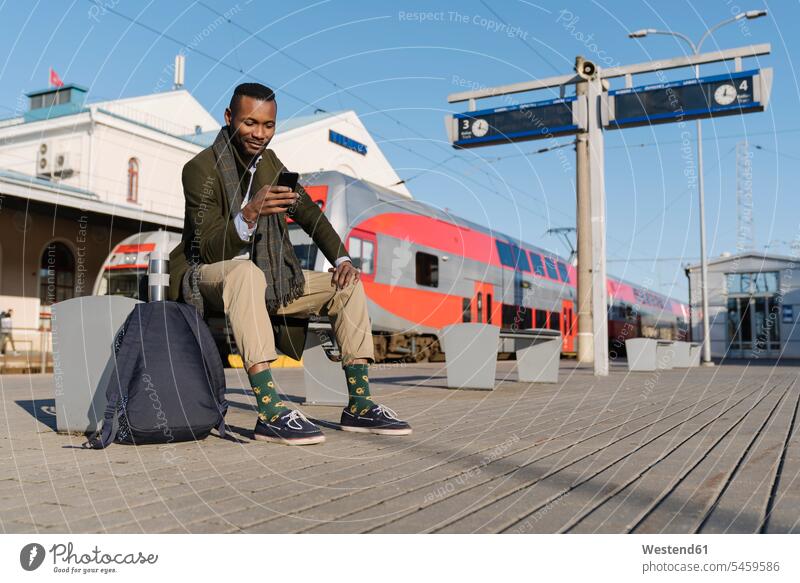 Stylischer Mann benutzt Smartphone beim Warten auf den Zug geschäftlich Geschäftsleben Geschäftswelt Geschäftsperson Geschäftspersonen Businessmann